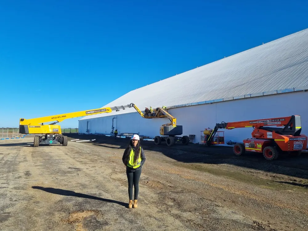 Nikita Gossain in hi-vis and a hard hat on site beside a large storage shed