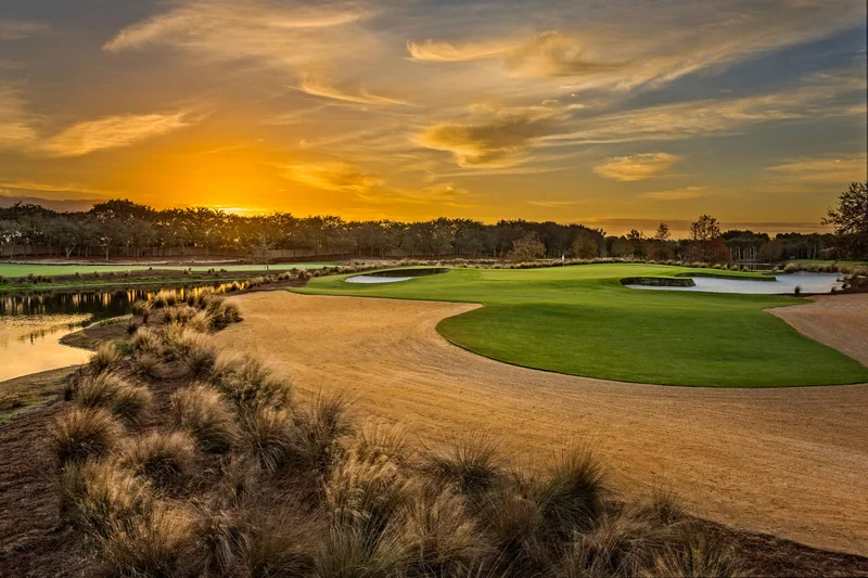 A golf course fairway and green under a rich golden sunset sky