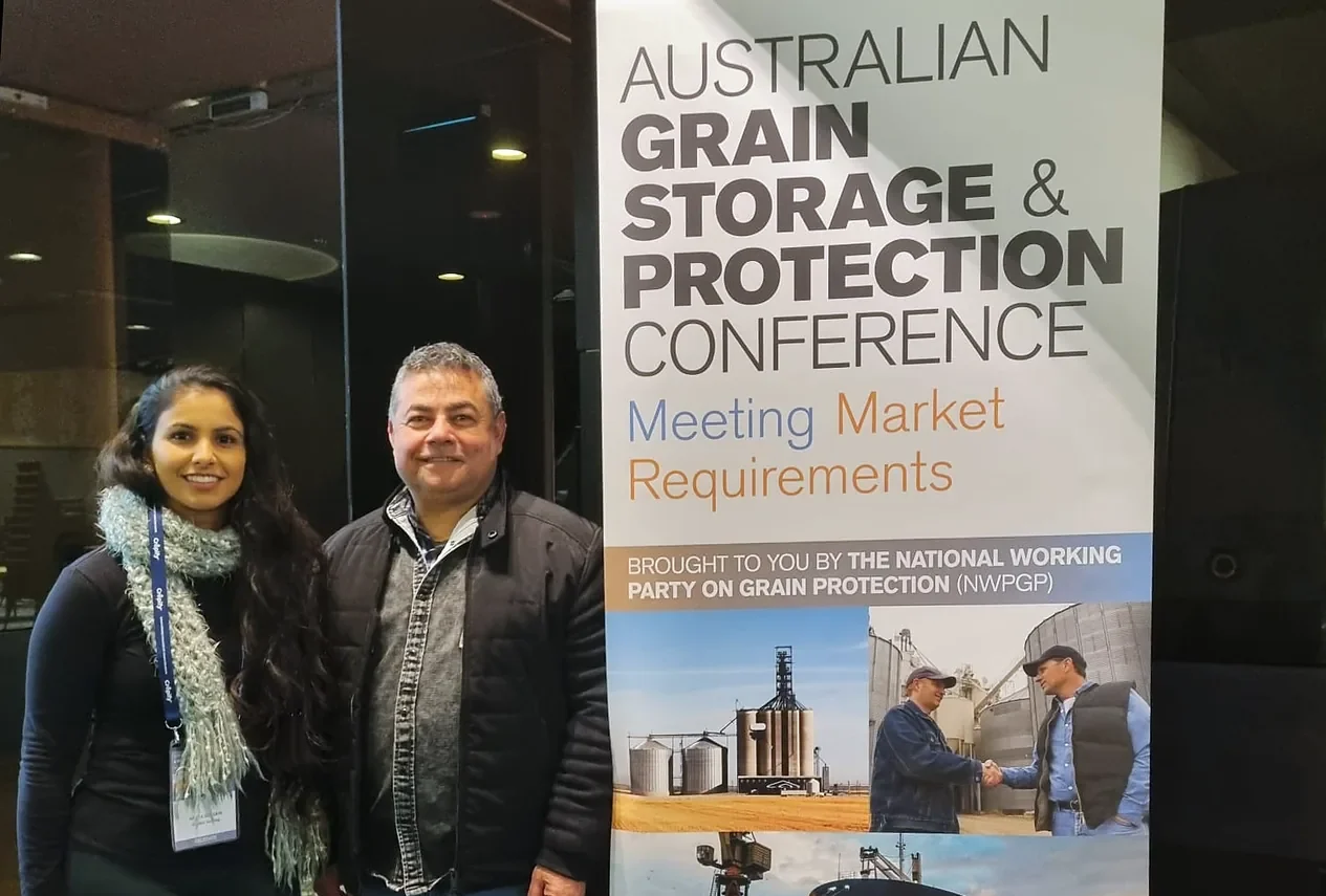 Nikita Gossain standing with a fellow attendee at the Australian Grain Storage and Protection Conference, beside the conference banner